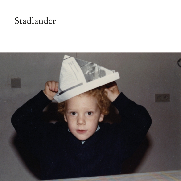 Albumhoes van Stadlander: foto van jong kindje dat papieren hoed opzet